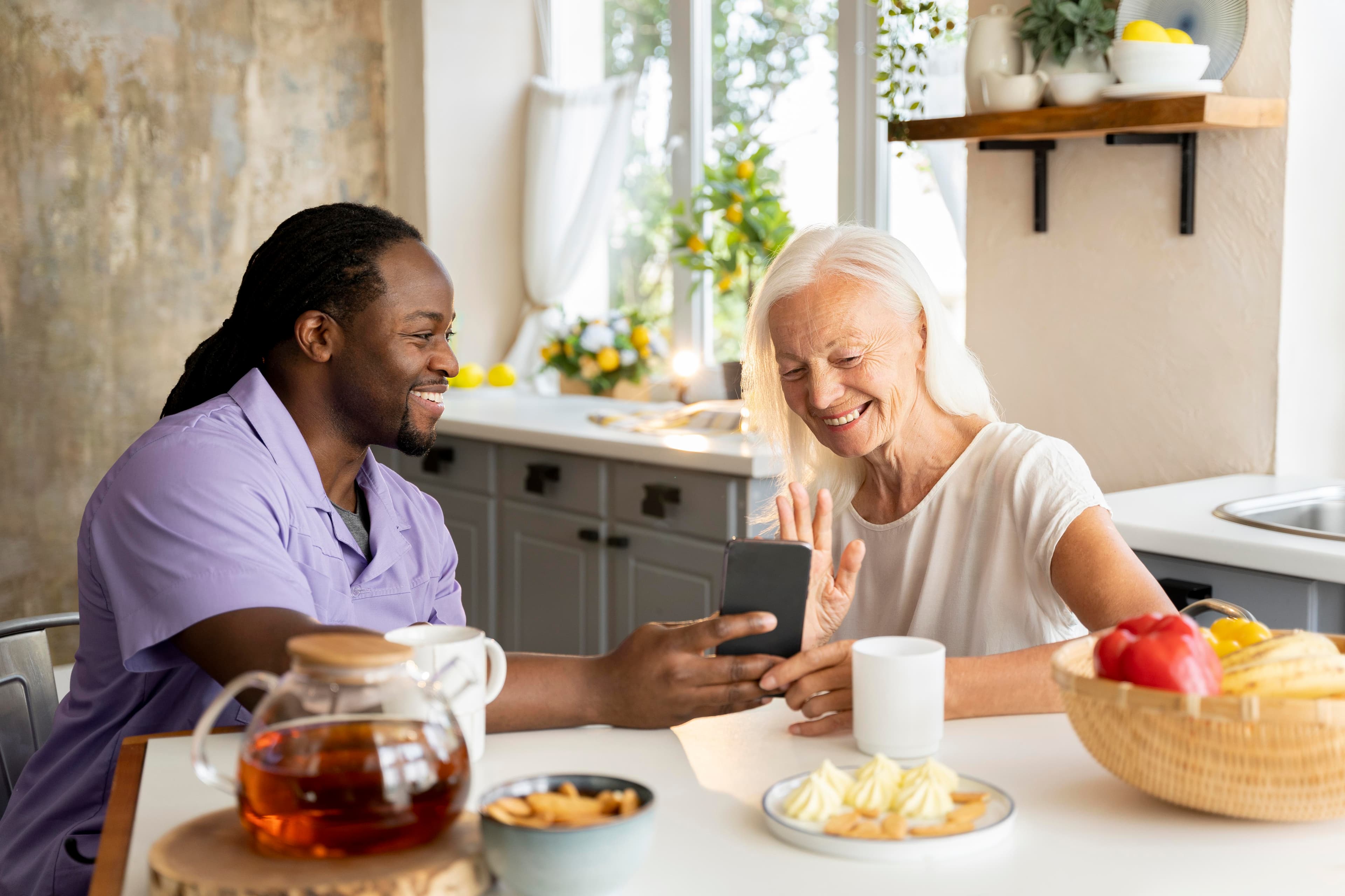 Caregiver and senior woman sharing a phone together at the kitchen table
