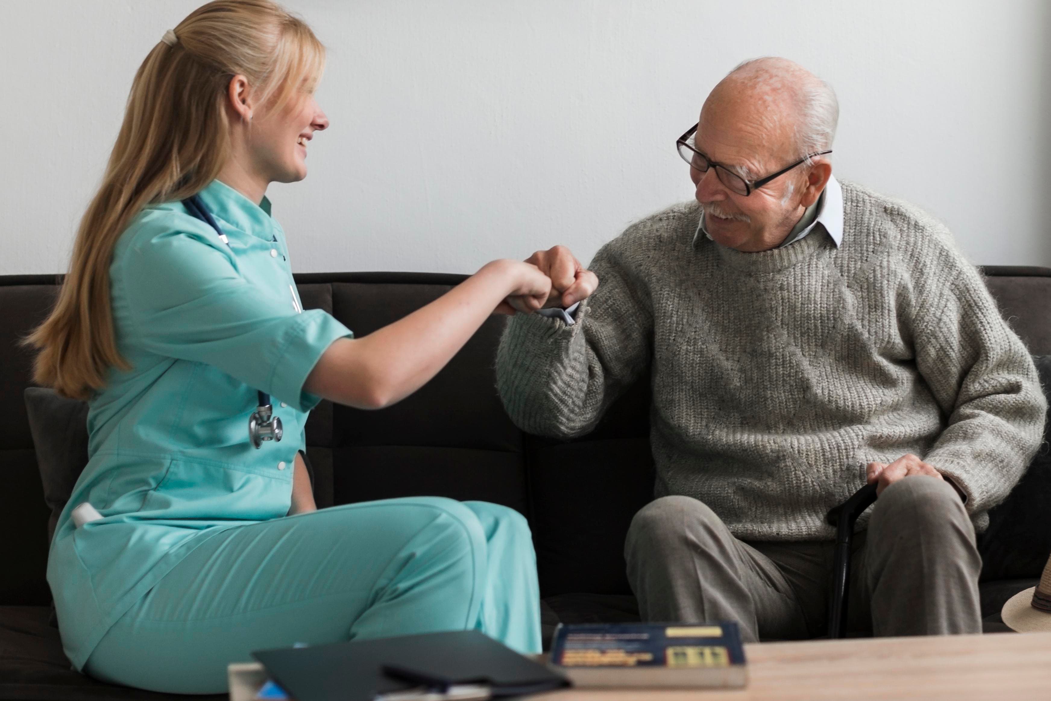 Caregiver and senior man sharing a friendly fist bump at home